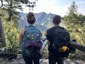 Clarice and her husband looking out over mountains in their hiking backpacks. 